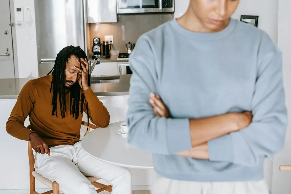 A distressed woman at a table while her partner stands nearby