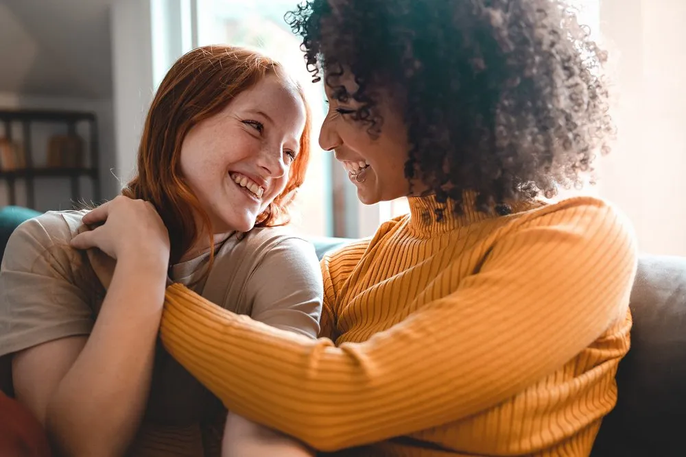 Two people smiling and hugging in a sunlit room