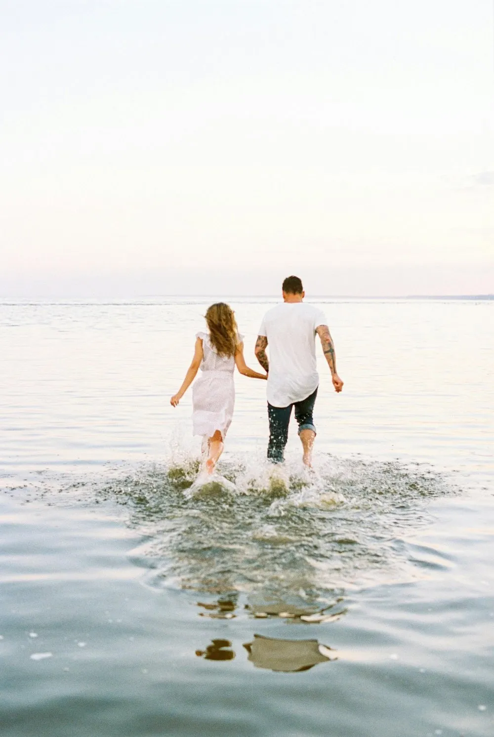 A couple holding hands and running in the water at the beach